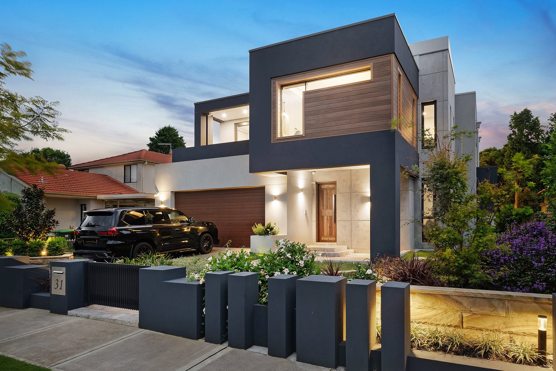 Alexander Avenue residence, modern facade with warm exterior lighting, timber accents, and landscaped entry at dusk.
